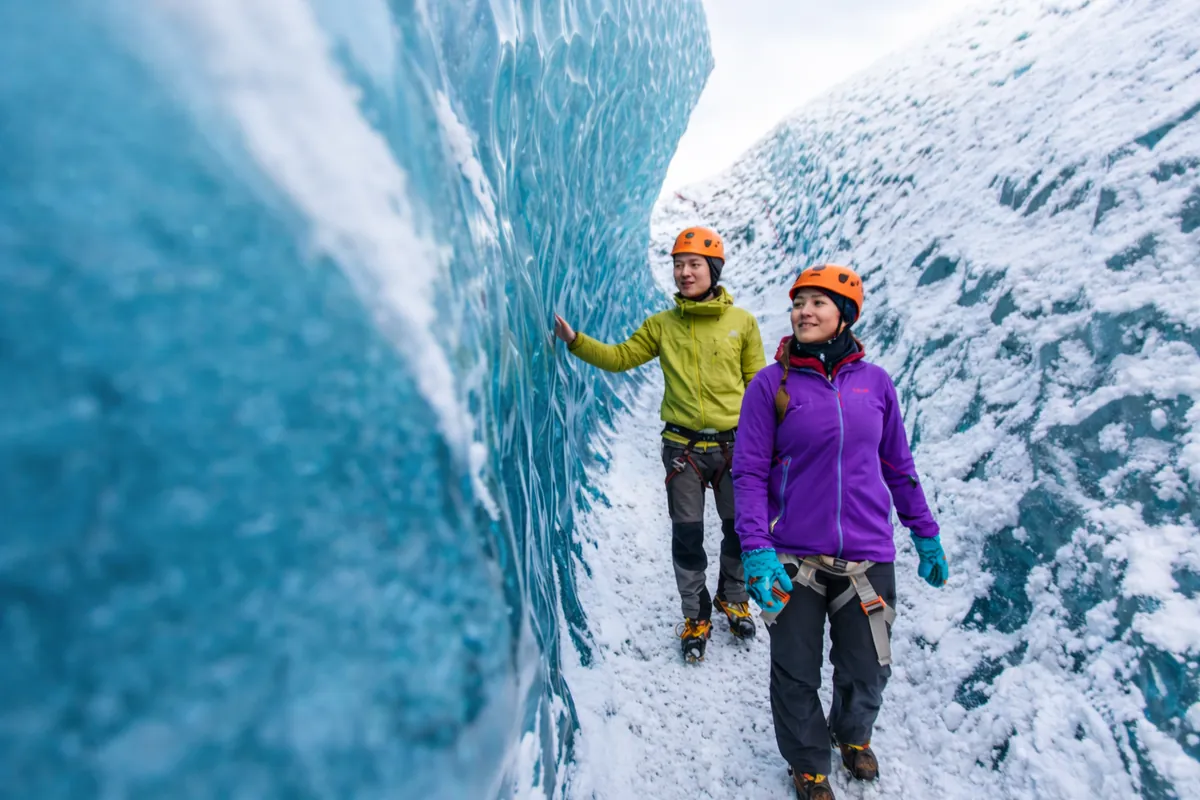 Two hikers with helmets walking through a narrow blue ice crevasse on a Vatnajökull outlet glacier