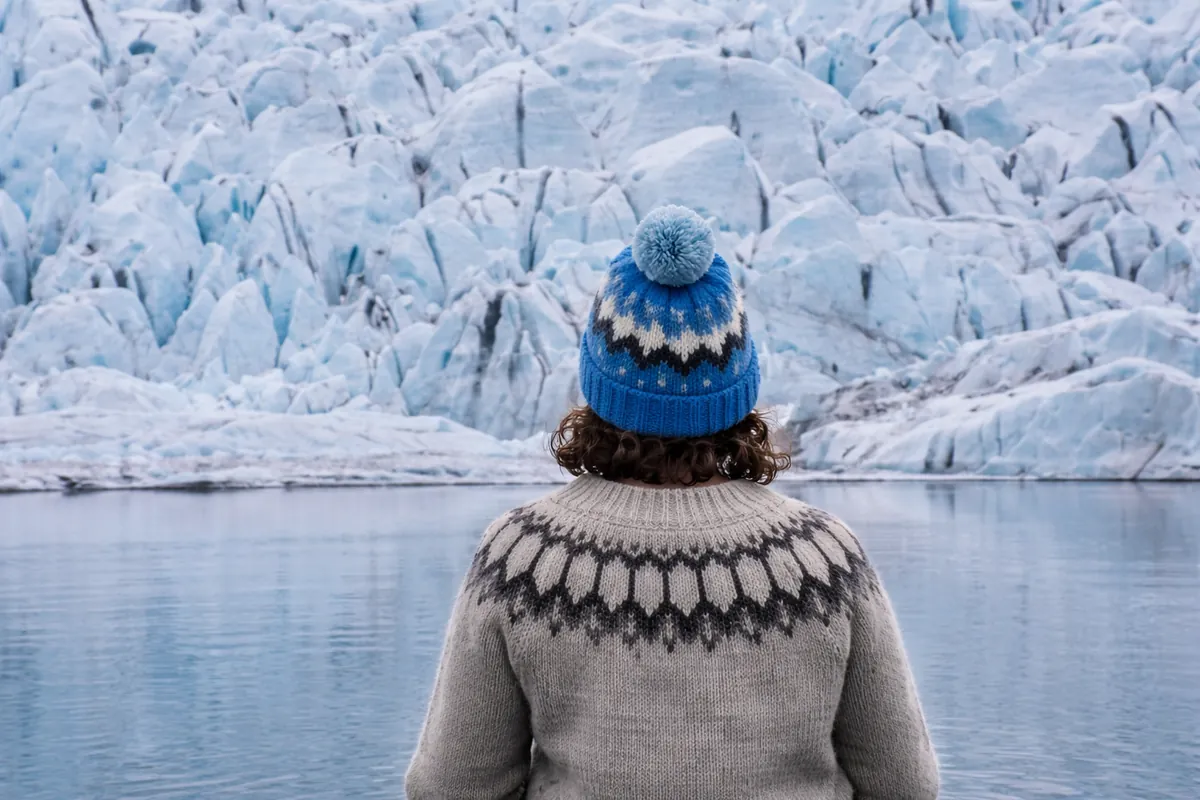 Visitor in an Icelandic sweater looking at the Fjallsjökull glacier wall across Fjallsárlón lagoon